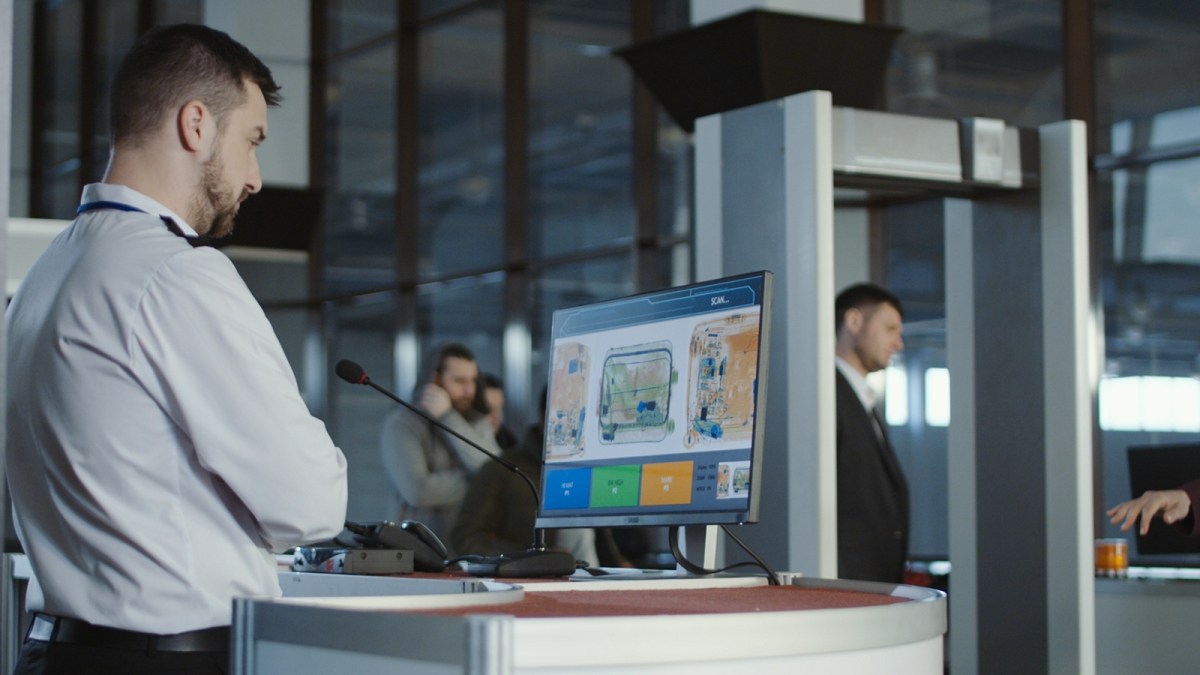 Un agent de sûreté aéroportuaire analysant l’écran d’un scanner de bagages à rayons X, assurant le contrôle et la sécurité des passagers en zone d’inspection filtrage.